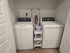 Une buanderie équipée de deux machines à laver à chargement frontal blanches, d’un étendoir blanc et d’un panier contenant de la lessive et une bouteille de détergent.