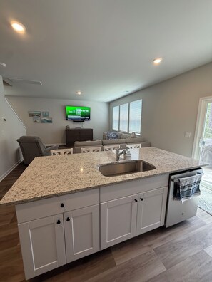 A modern kitchen with a granite countertop, white cabinetry, and a built-in dishwasher. - Live Love Your North Myrtle Beach Vacation - North Myrtle Beach (North Myrtle Beach)