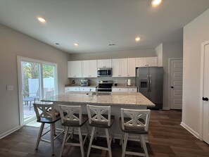 A modern kitchen with white cabinets, a stainless steel refrigerator, and a granite countertop. - Live Love Your North Myrtle Beach Vacation - North Myrtle Beach (North Myrtle Beach)