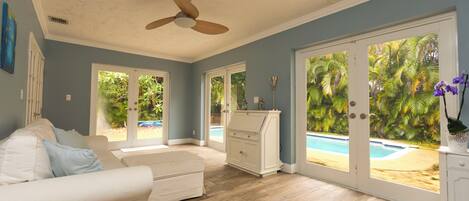 A spacious living room with a ceiling fan, a white sofa, and a view of a swimming pool through large glass doors.
