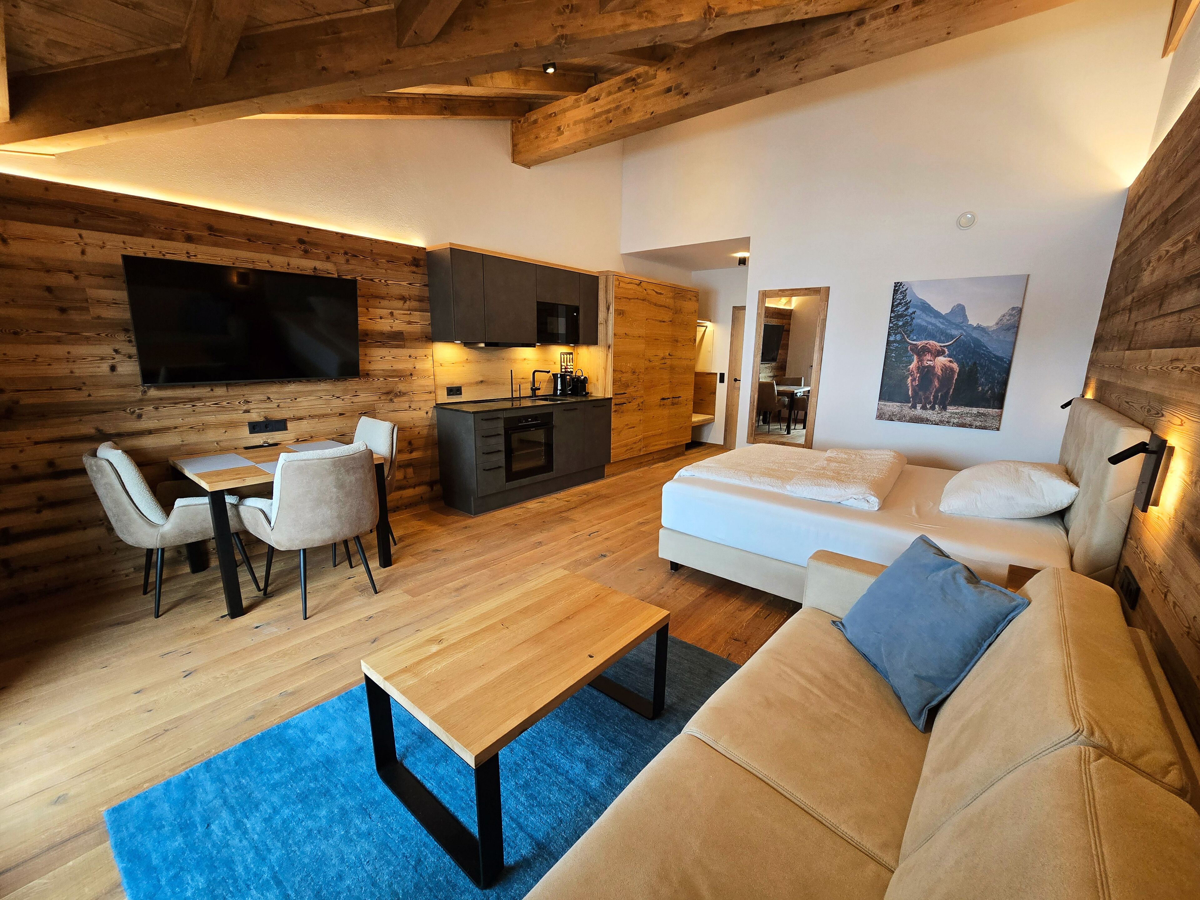 Un interior moderno con techo de madera, comedor, kitchenette, sofá y un televisor plano grande.