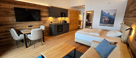 Un interior moderno con techo de madera, comedor, kitchenette, sofá y un televisor plano grande.