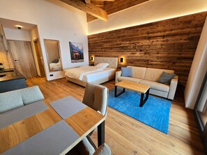 Een moderne hotelkamer met een houten plafond, een bed, een sofa, een salontafel en een eethoek met een tafel en stoelen.
