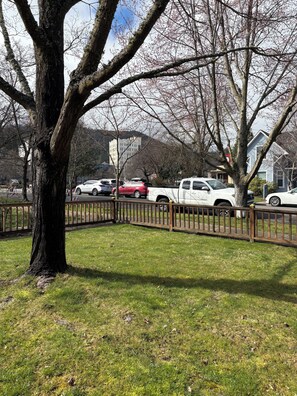 A parking area with a tree in the foreground, a fence, and several parked cars. - Stacy’s 2nd st cottages front house (Ashland)