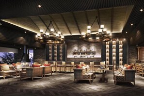 A spacious lounge area with multiple seating options, a bar with a variety of bottles, and a large window providing a view. - Dusit Thani Himalayan Resort (Dhulikhel)