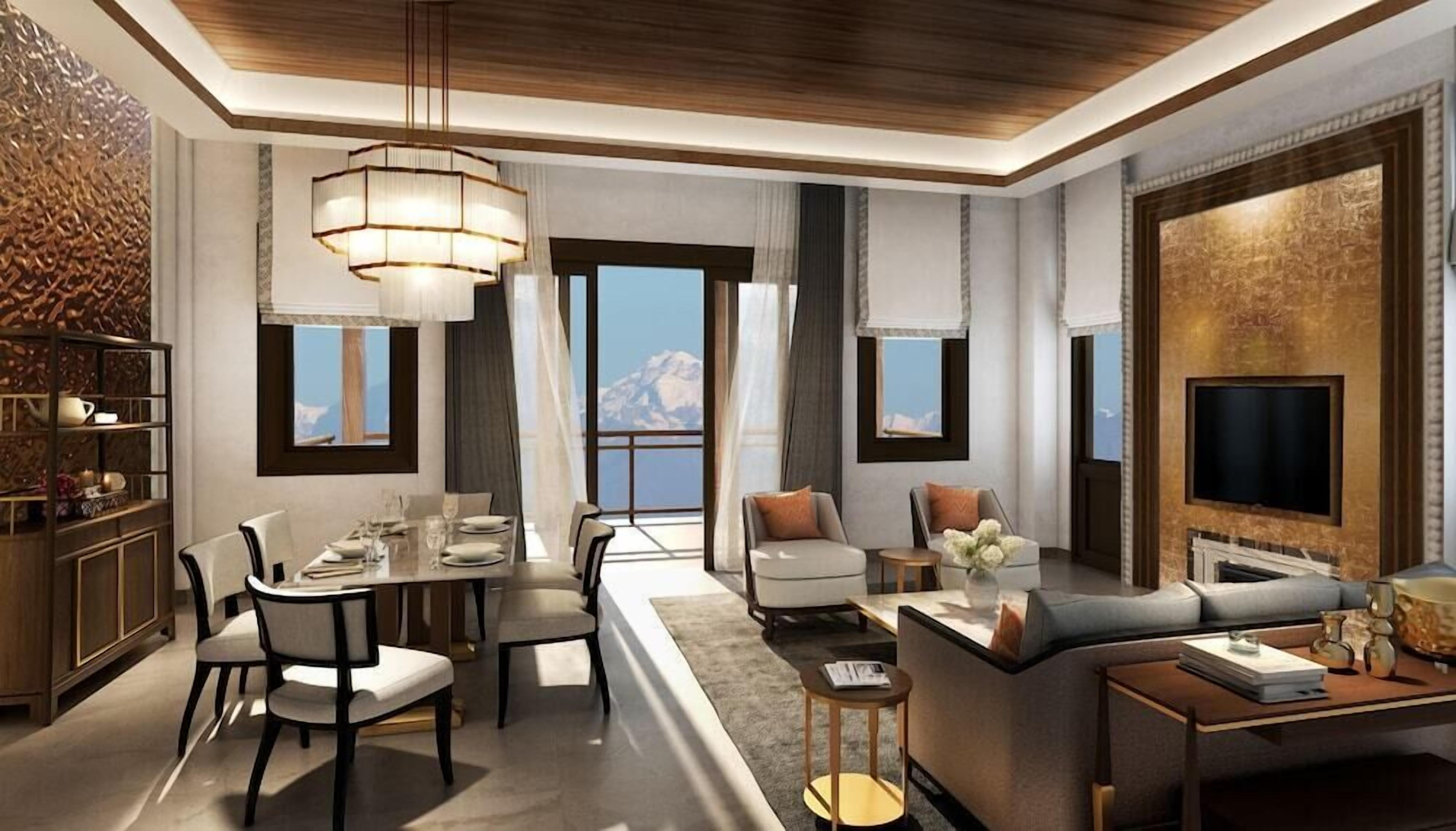 A modern living room with a dining area, a sofa set, a TV mounted on a wall, and a view of the mountains.