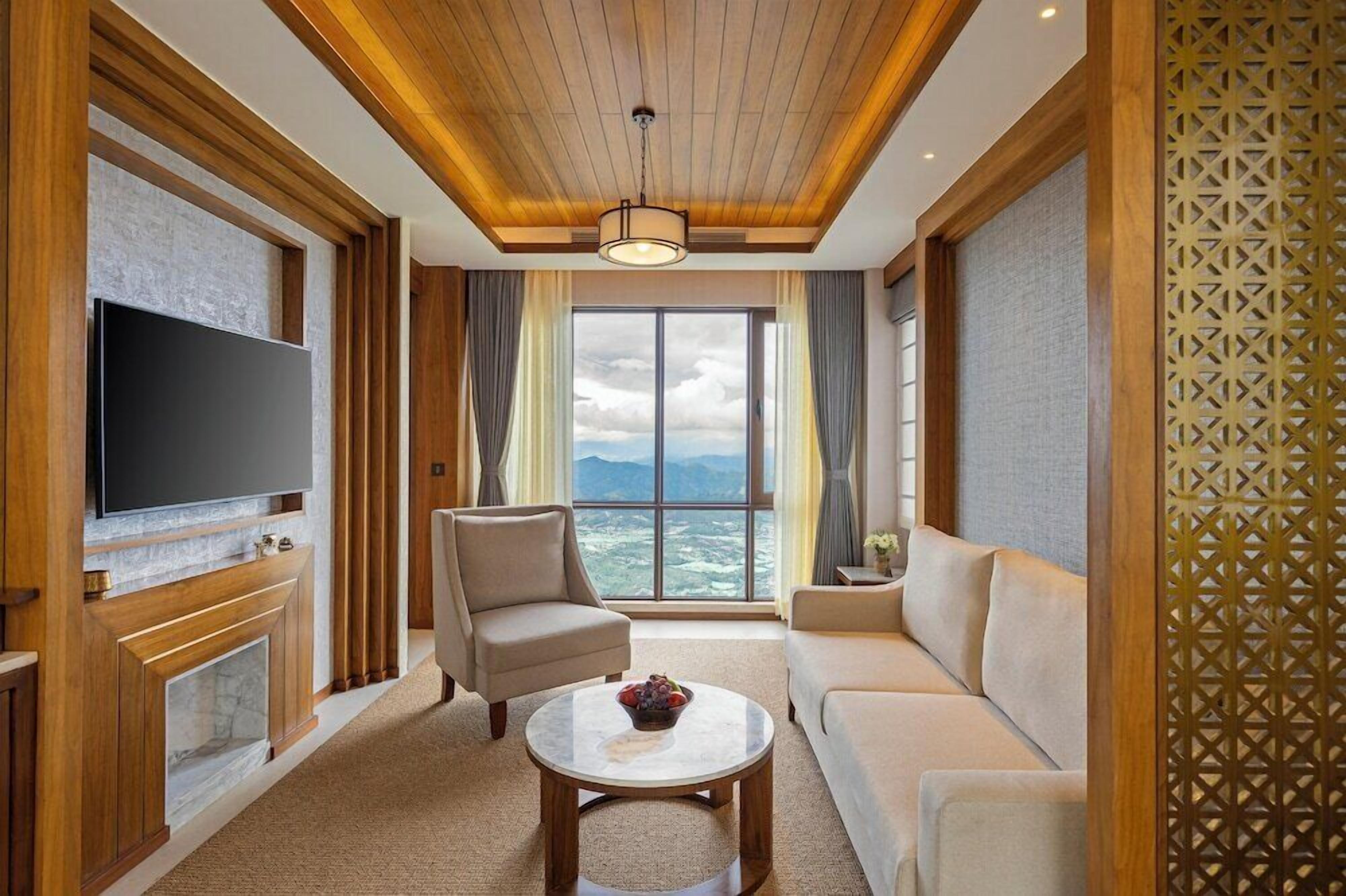 A modern living room with a flat-screen TV, a fireplace, a sofa, and a large window offering a view of the outdoors.