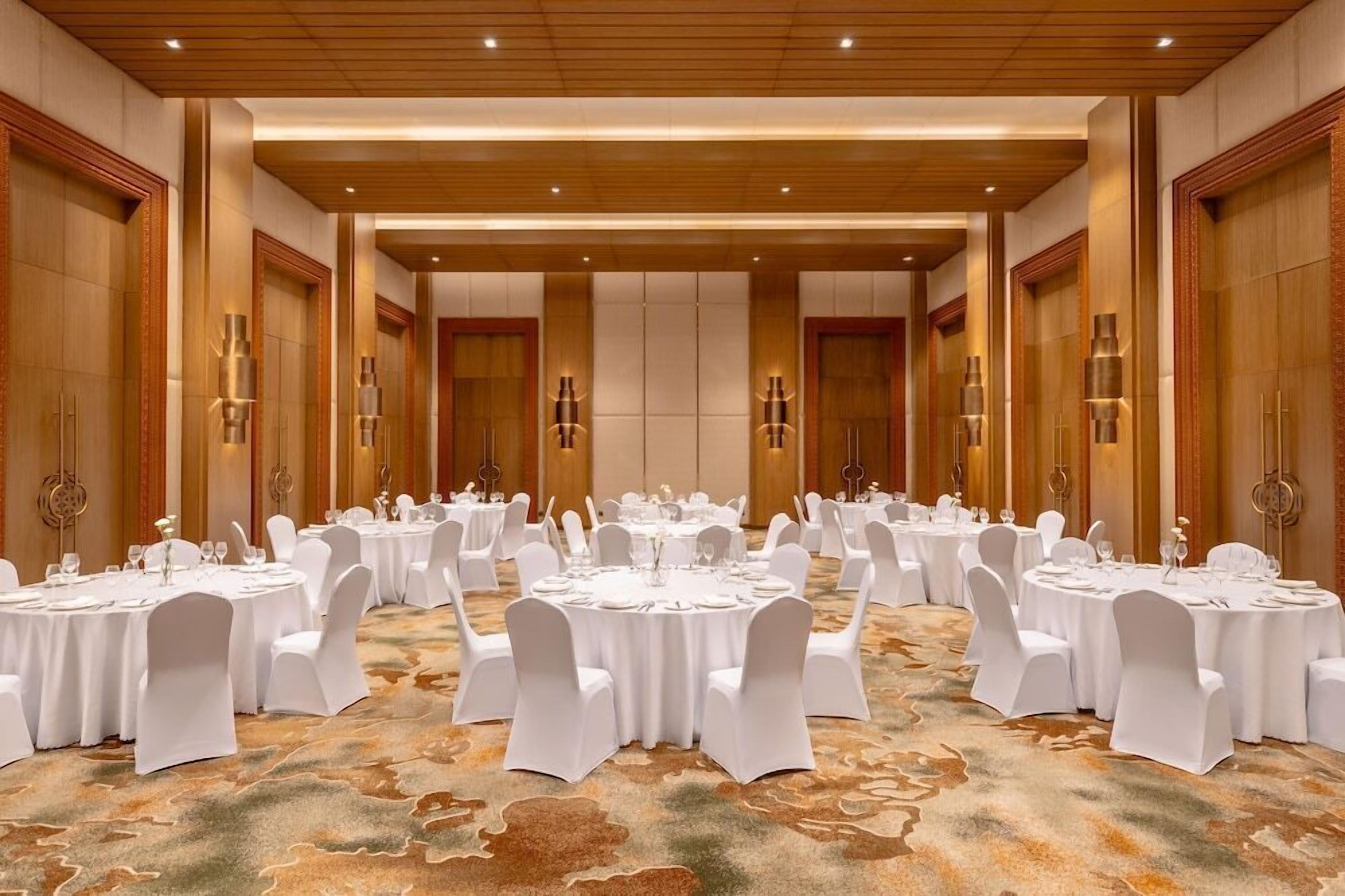 A banquet hall with round tables and white chairs, wooden paneling, and wall sconces.