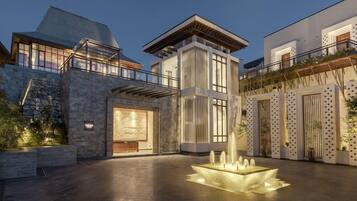 A modern building with a stone facade, a central courtyard with a water feature, and a balcony with plants.