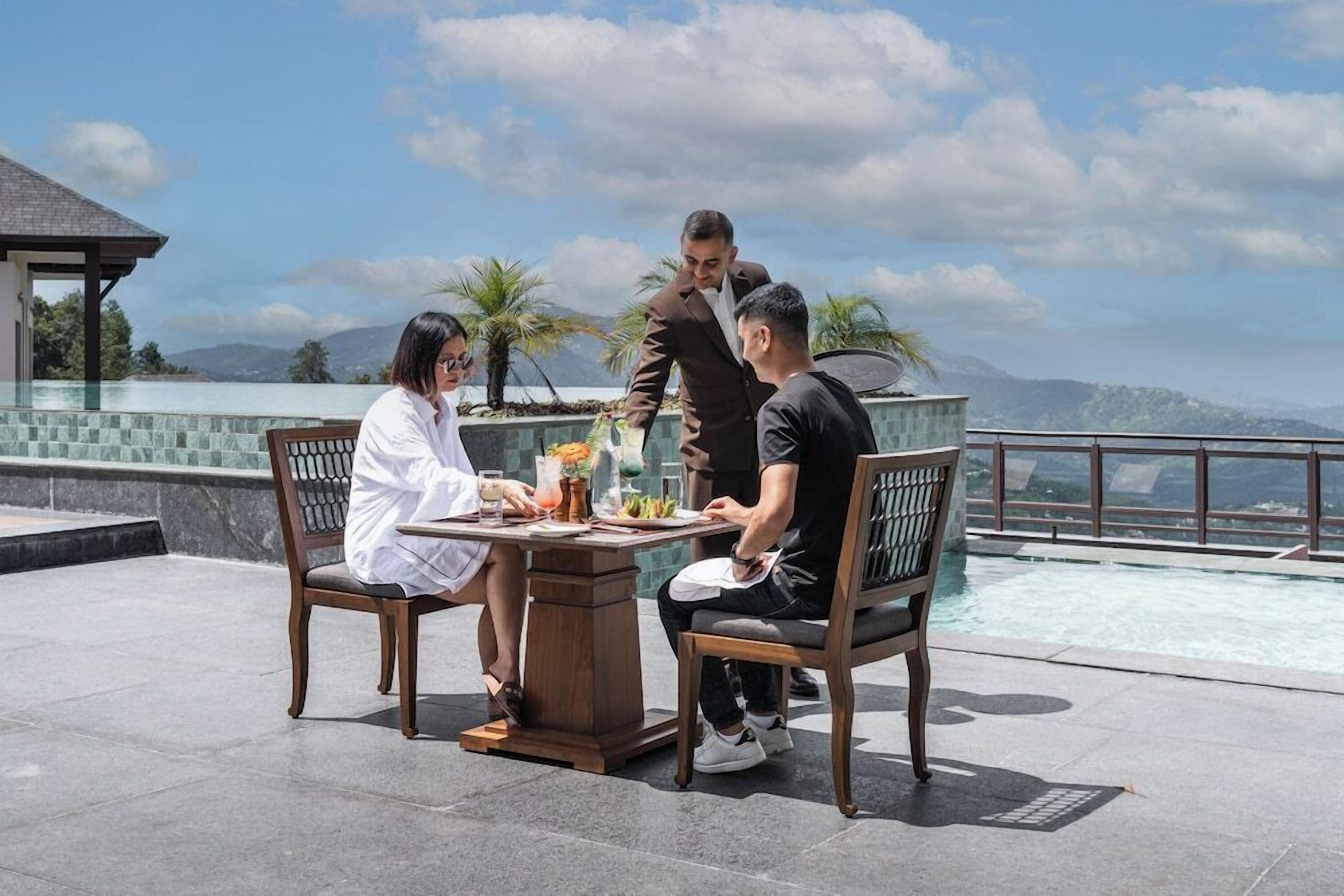 A dining area with a table, chairs, and a view of a swimming pool and mountains.