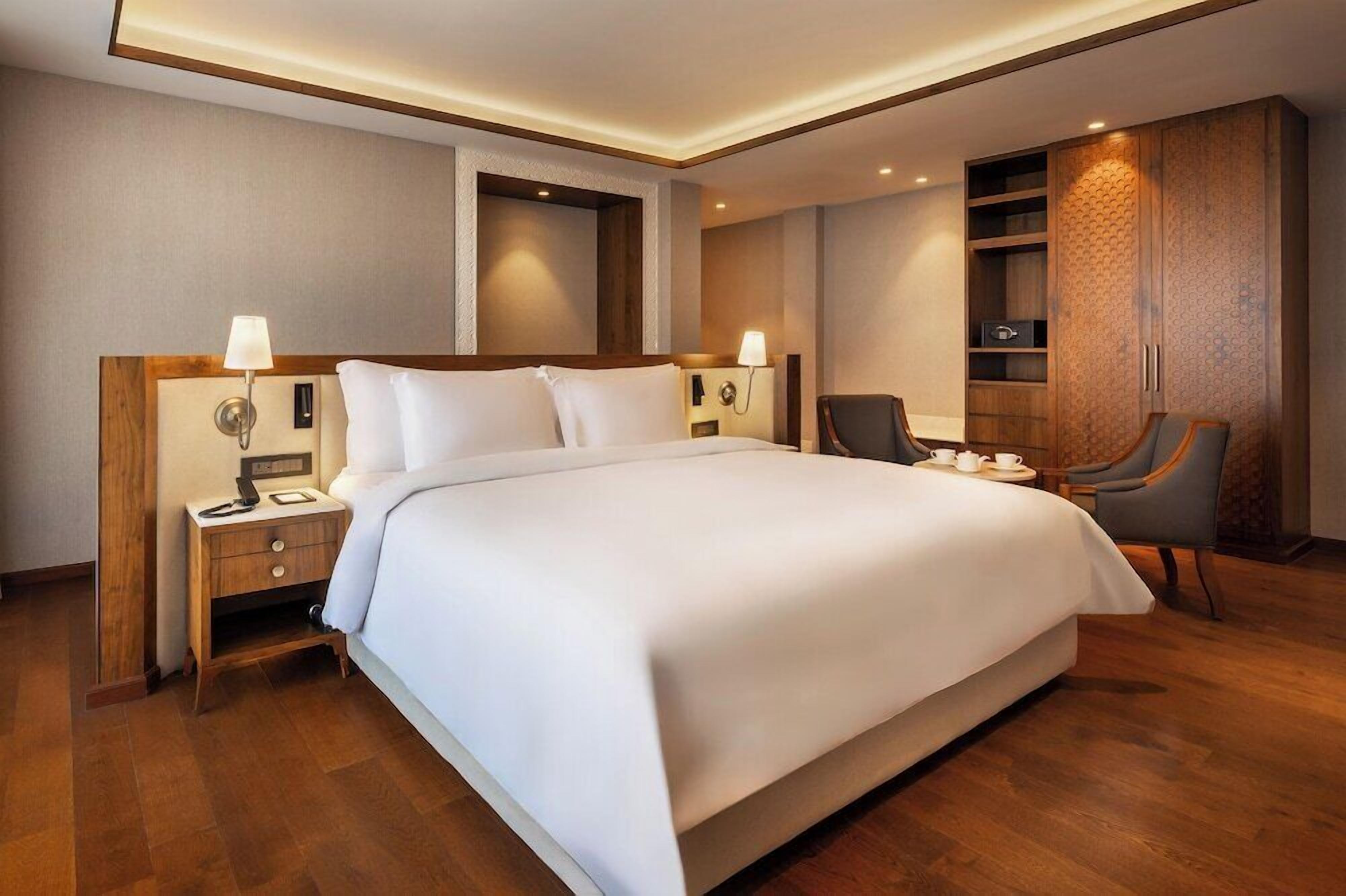 A hotel room with a large bed, bedside lamps, a desk, a chair, and a wardrobe.