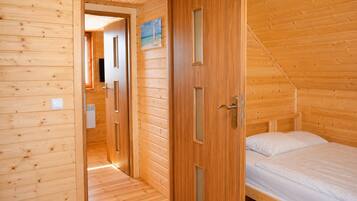 A wooden interior with a bed, a door, and a hallway leading to another room.