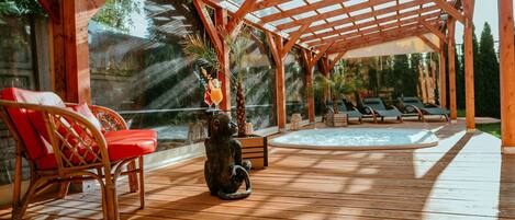 Une terrasse en bois avec une véranda vitrée, un espace salon extérieur et un jacuzzi.