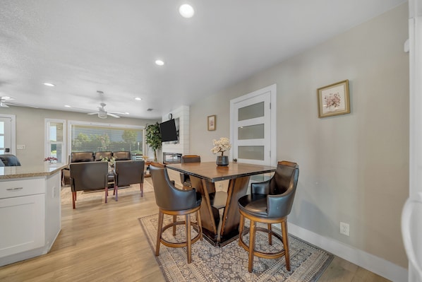 A modern kitchen with a dining area, wooden flooring, and a ceiling fan.