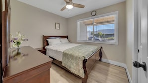 Un dormitorio con cama, ventilador de techo, ventana con persianas y un reloj en la pared.