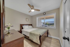 A bedroom with a bed, a ceiling fan, a window with blinds, and a clock on the wall.