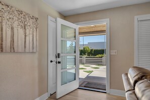 An open door leading to a balcony with a view of the outdoors, a modern interior with a light-colored wall, and a piece of abstract art on the wall. - Walk to dining & shopping Spacious 3 BR home With large yard and pool. (Ceres)
