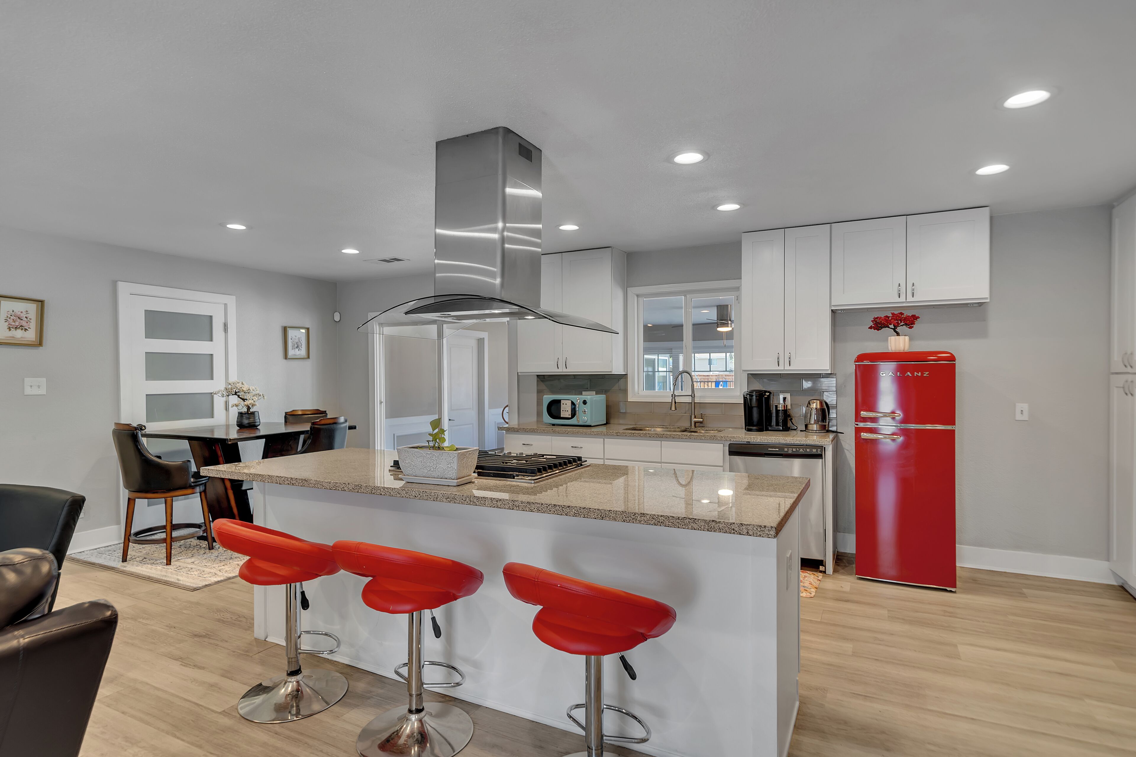 A modern kitchen with a central island, bar stools, and a red refrigerator.