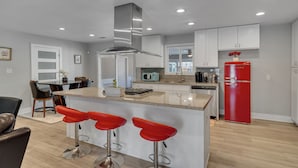 Una cocina moderna con una isla central, taburetes de bar y un refrigerador rojo.
