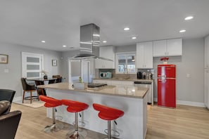 A modern kitchen with a central island, bar stools, and a red refrigerator.