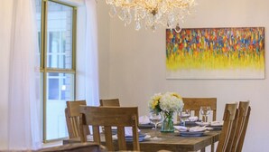 Una sala da pranzo con un lampadario, un tavolo apparecchiato per sei persone e un colorato quadro astratto appeso al muro.