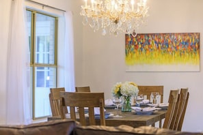 Ein Esszimmer mit einer Chandelierleuchtre, einem für sechs Personen gedeckten Tisch und einem farbenfrohen, abstrakten Gemälde an der Wand.