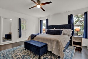 A bedroom with a large bed, a ceiling fan, a nightstand, and a window with curtains.