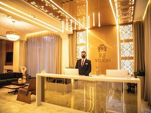 A reception desk with a man standing behind it, a chandelier, and a wall with a logo. - Hotel RF Vision Restaurante Giratorio (Gramado)