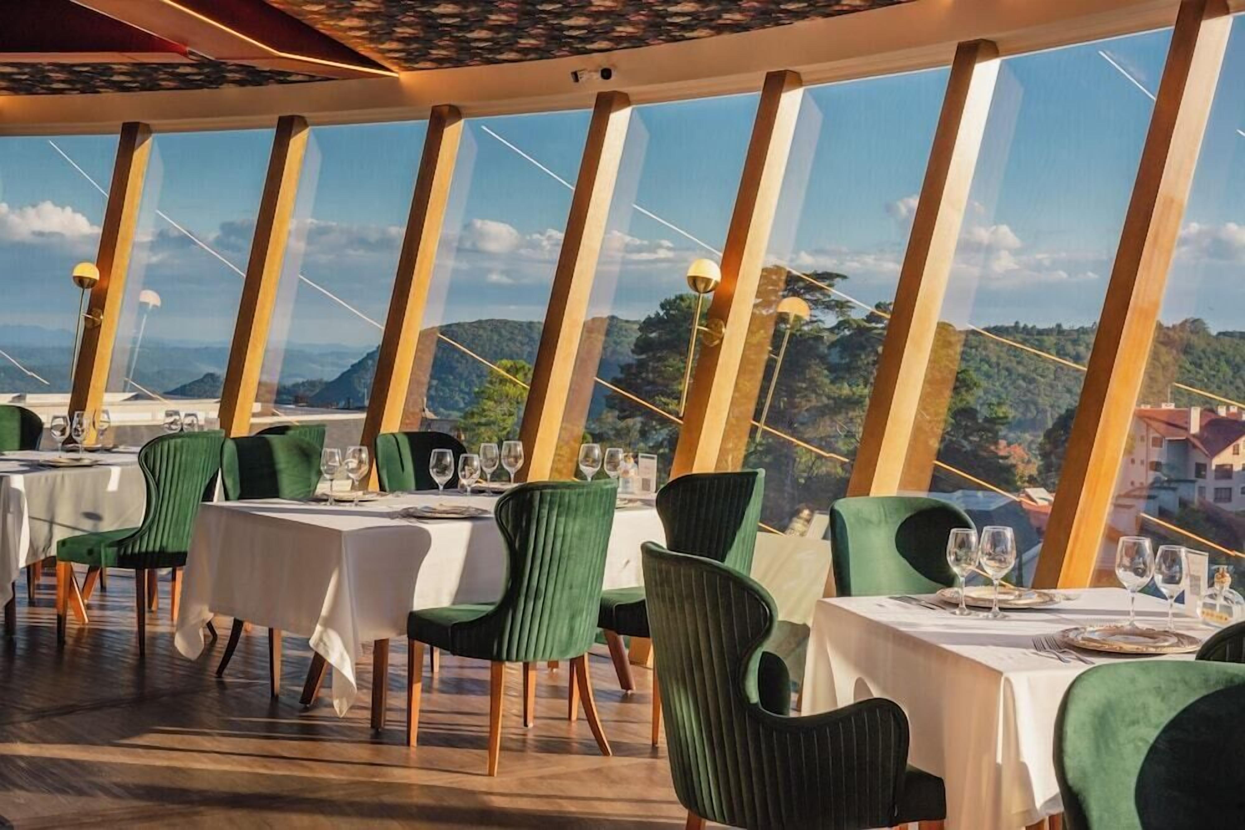 A restaurant with tables set for dining, featuring a view of a mountainous landscape through large windows.