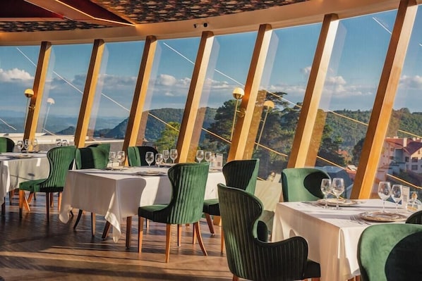 A restaurant with tables set for dining, featuring a view of a mountainous landscape through large windows. - Hotel RF Vision Restaurante Giratorio (Gramado)