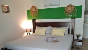 Ein Schlafzimmer mit einem Bett, einem Deckenventilator, einer Klimaanlage und einem kleinen Nachttisch mit Pflanze.