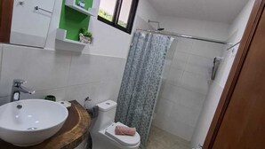 Ein Badezimmer mit Waschbecken, Toilette, Dusche und einer kleinen Stufe zum Duschbereich.