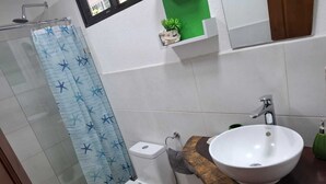 Ein Badezimmer mit Dusche, Toilette, Waschbecken und einem kleinen Regal mit einer Pflanze.