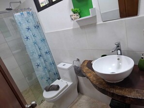 Ein Badezimmer mit Dusche, Toilette, Waschbecken und einem kleinen Regal mit einer Pflanze.