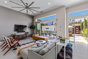 A modern living room with a sofa, coffee table, TV, and a dining area with chairs and a table. - Play and Stay Sanctuary - Detached Casita + Pickleball + Putting Green • Casita + 4 Kings (Palm Springs)