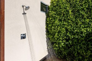 A wall-mounted showerhead and a small control panel, adjacent to a dense green hedge. - Play and Stay Sanctuary - Detached Casita + Pickleball + Putting Green • Casita + 4 Kings (Palm Springs)