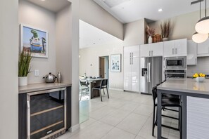 A modern kitchen with stainless steel appliances, a dining area with a table and chairs, and a large island with a bowl of lemons. - Play and Stay Sanctuary - Detached Casita + Pickleball + Putting Green • Casita + 4 Kings (Palm Springs)