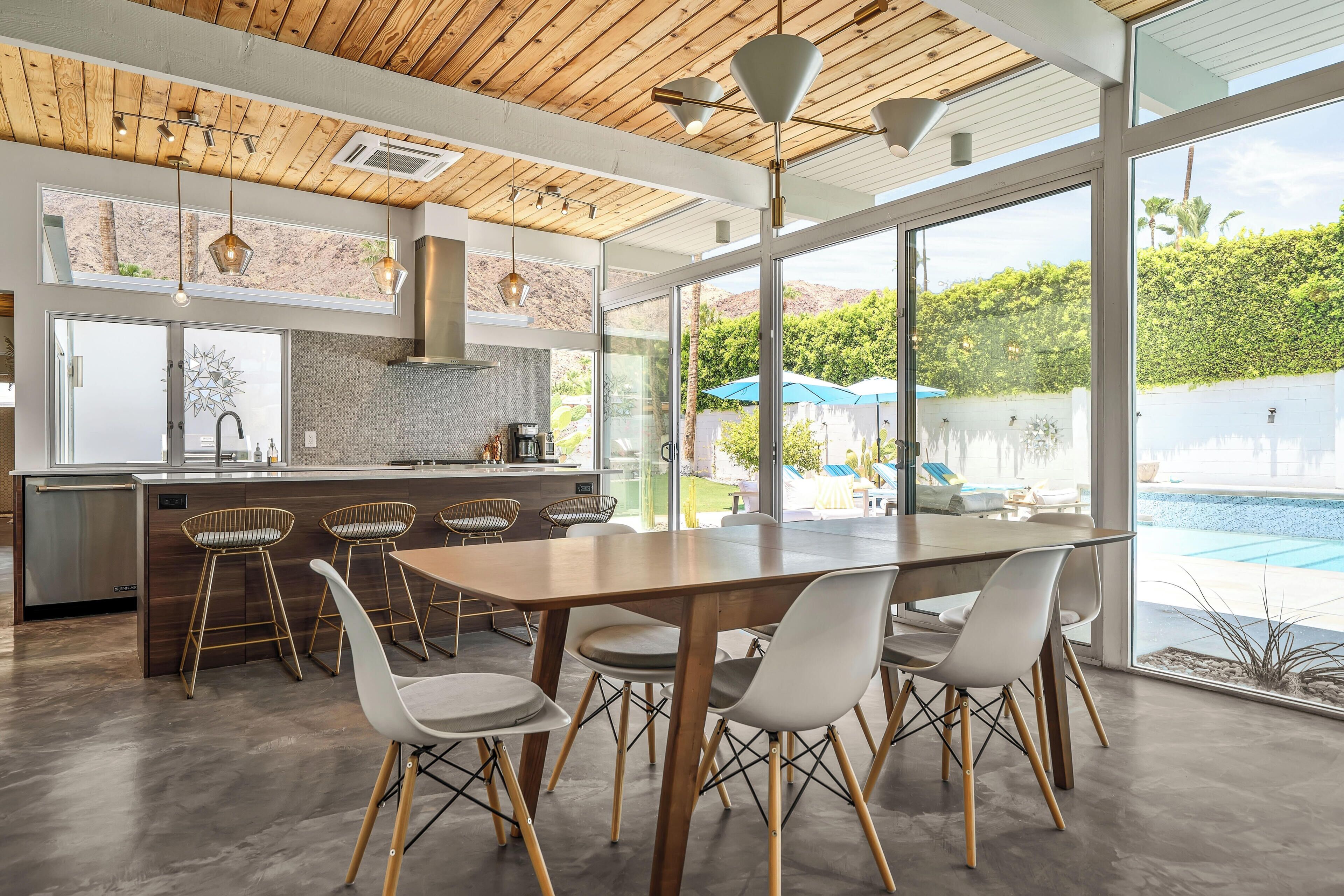 A modern kitchen with a large island, bar stools, and a dining area with a view of a swimming pool.