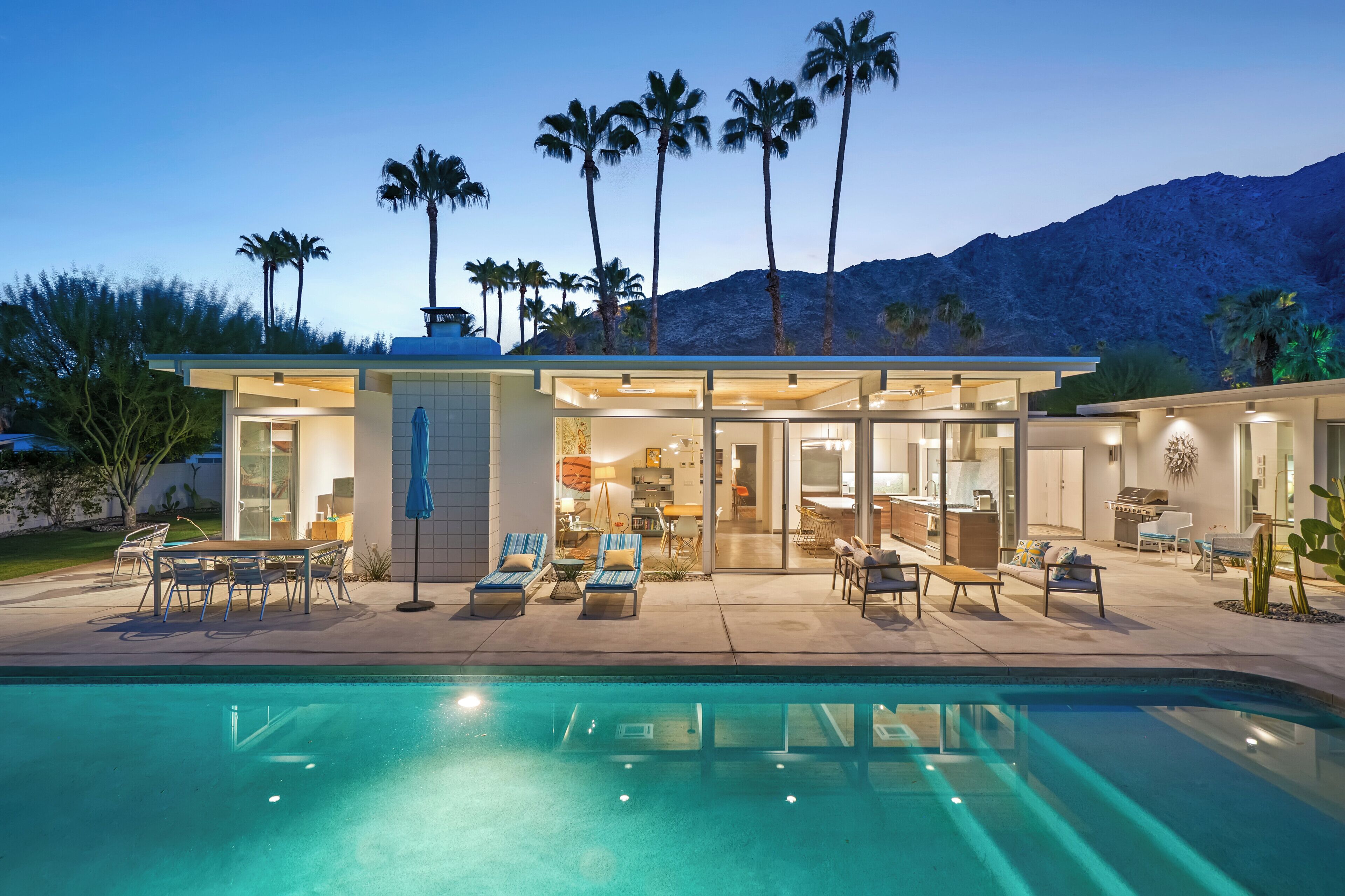 A modern house with a pool, outdoor seating, and palm trees.