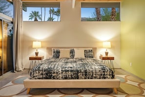 A bedroom with a large bed, two bedside tables, and a view of palm trees through the windows. - No Paparazzi - Palm Springs Paradise: Your Private Poolside Retreat Awaits (Palm Springs)
