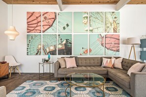 A modern living room with a sectional sofa, a glass coffee table, and a large wall art installation depicting amusement park rides. - No Paparazzi - Palm Springs Paradise: Your Private Poolside Retreat Awaits (Palm Springs)