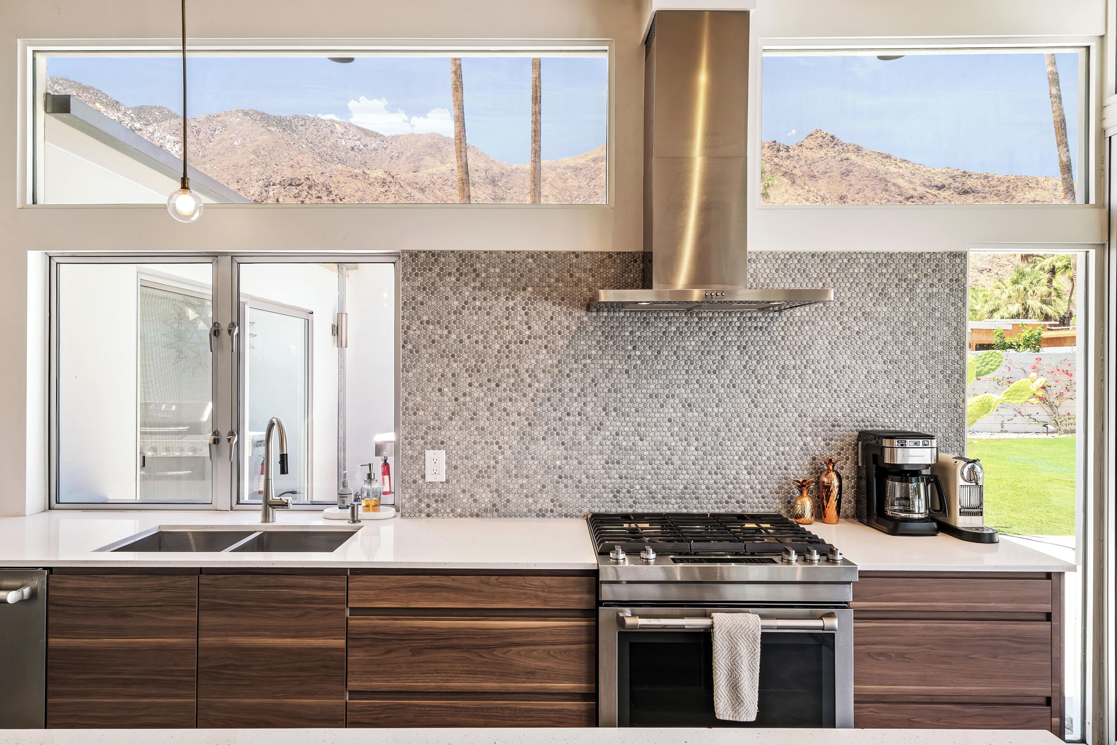 A modern kitchen with a stainless steel range, a built-in oven, and a large window overlooking a mountainous landscape.