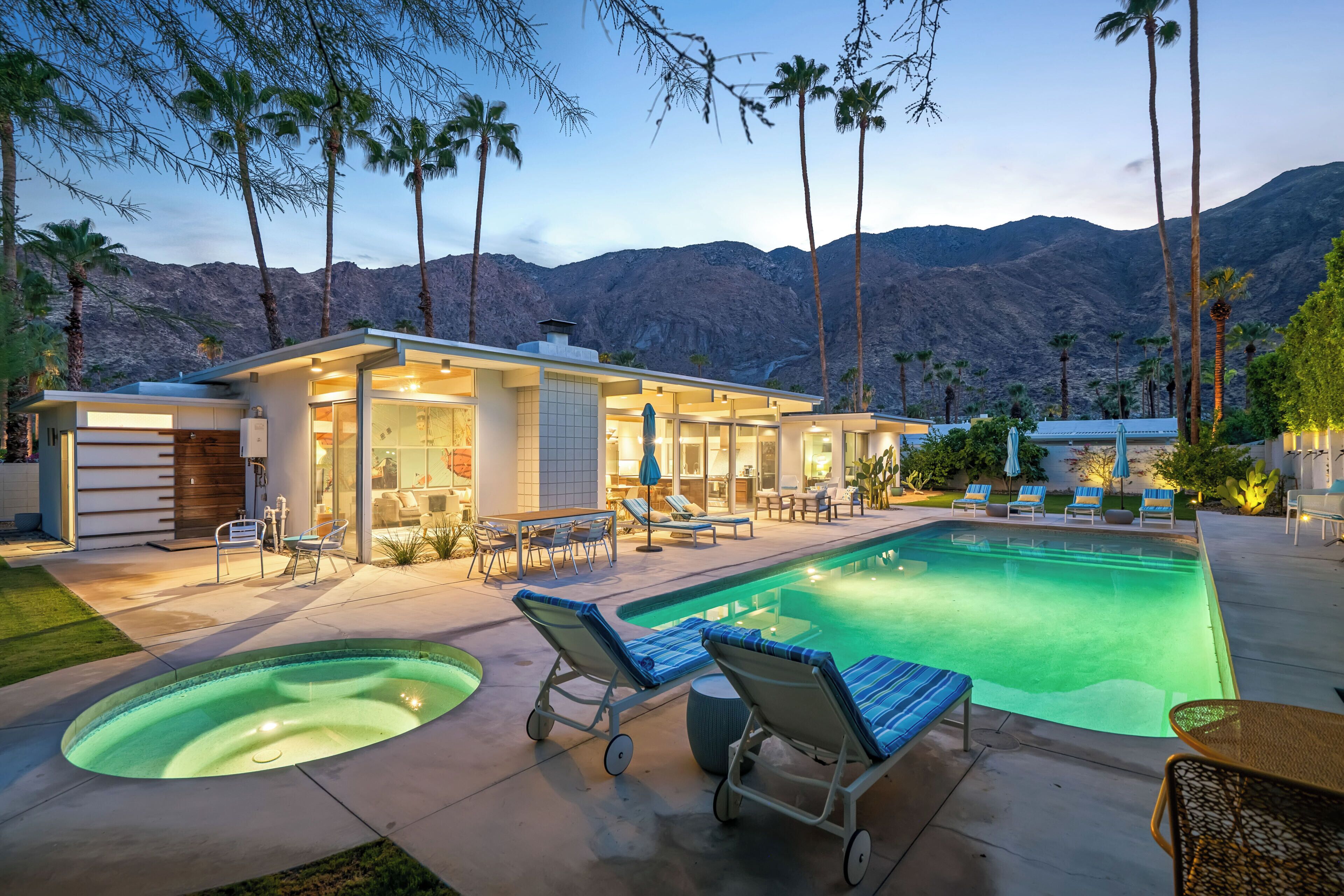 A modern house with a swimming pool, lounge chairs, and a mountain backdrop.