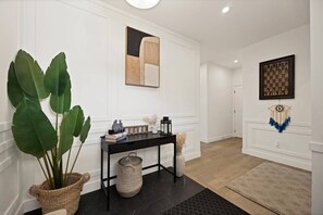 A hallway with a black console table, a large potted plant, a chessboard, and a dreamcatcher. - Upscale Show Home | Family House | Workspace (Calgary)
