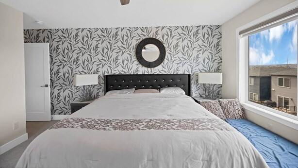 Een slaapkamer met een bed, een plafondventilator, een raam met uitzicht en behang met een patroon.
