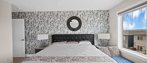 A bedroom with a bed, a ceiling fan, a window with a view, and patterned wallpaper.