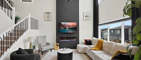 A modern living room with a staircase, a fireplace, a sofa, a coffee table, and a television.