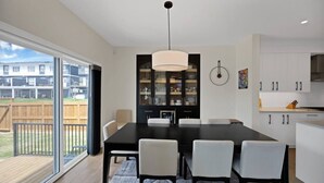 Een moderne keuken met een eethoek, grote ramen en uitzicht op een woonwijk.