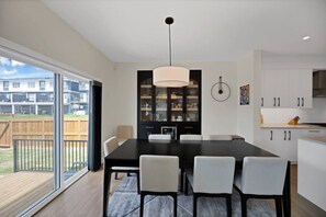 A modern kitchen with a dining area, large windows, and a view of a residential area. - Upscale Show Home | Family House | Workspace (Calgary)