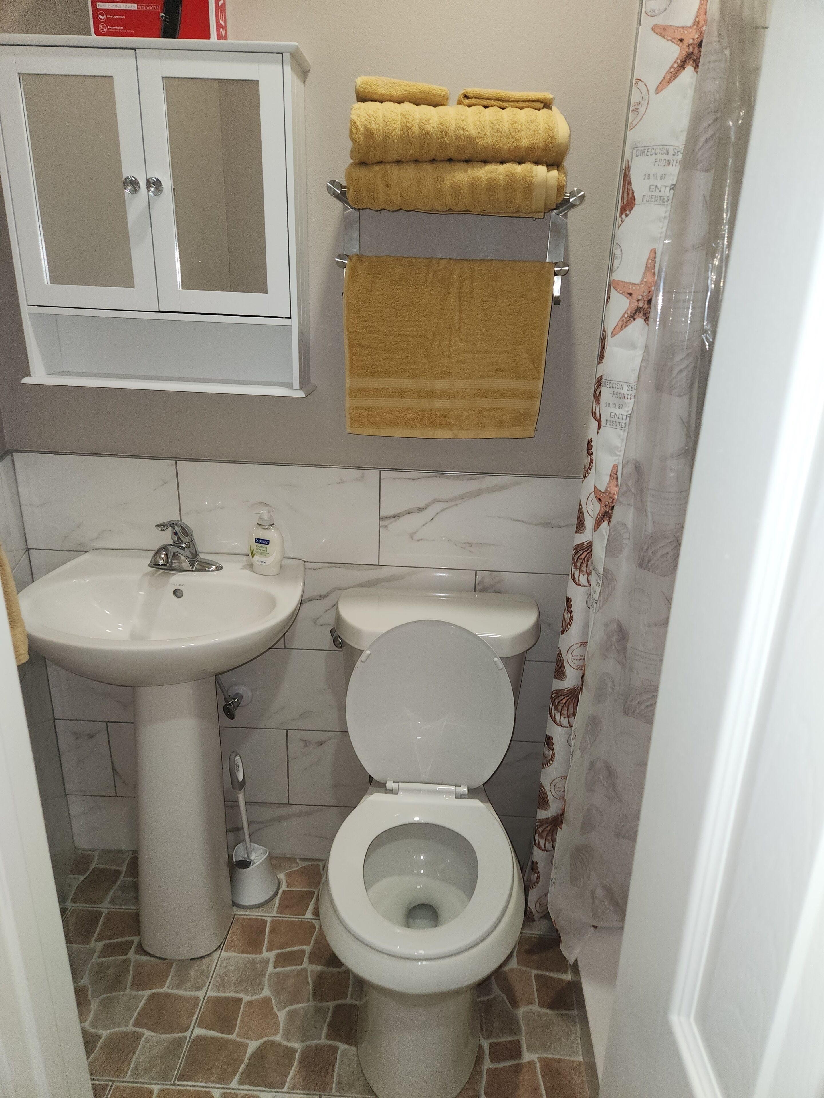 Une salle de bain avec un lavabo blanc, des toilettes et un meuble au-dessus du lavabo. Des serviettes sont posées sur un porte-serviettes au-dessus des toilettes.